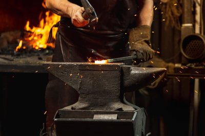 anvil with metal on it and man holding hammer 